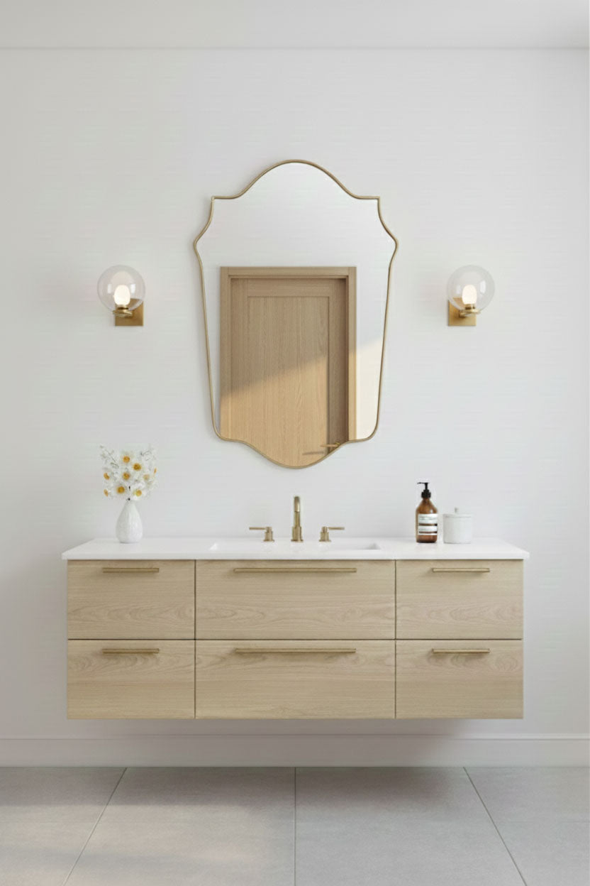 Shield-shaped gold mirror mounted above light wood bathroom vanity