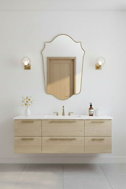 Shield-shaped gold mirror mounted above light wood bathroom vanity