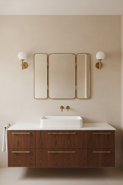 Foldable brass vanity mirror mounted above a bathroom sink with warm beige walls