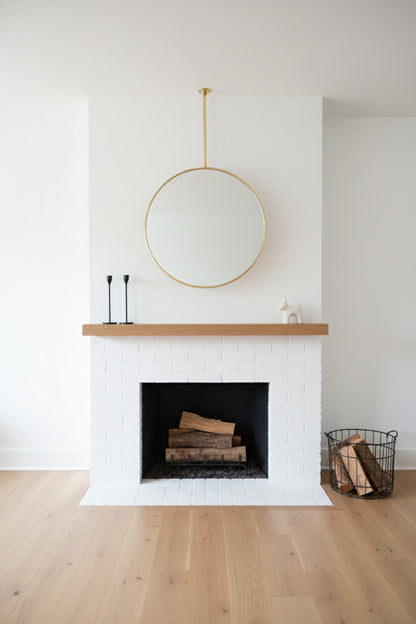 Round suspended brass mirror above a white brick fireplace